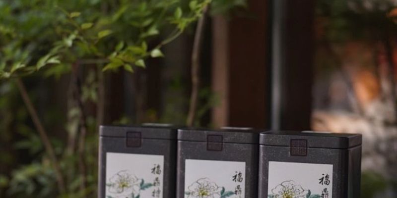 Three dark tins of white peony tea labeled in Chinese, lined up on a table against a blurred garden