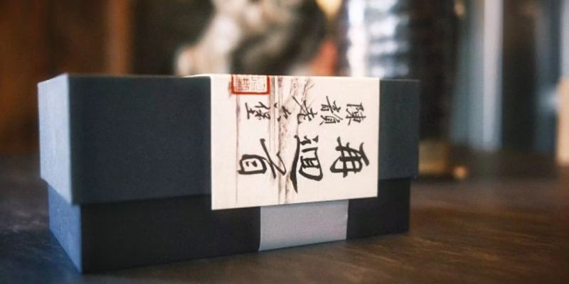 A dark gift box with a calligraphy-printed paper wrap, set on a wooden table