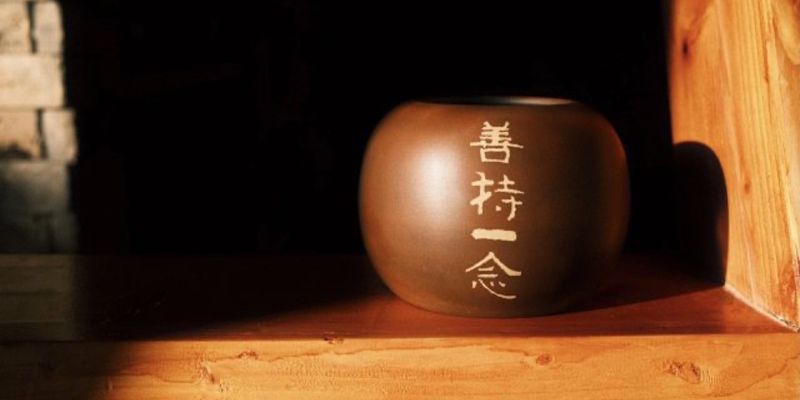 A dark clay water vessel inscribed with four characters, lit by a shaft of window light