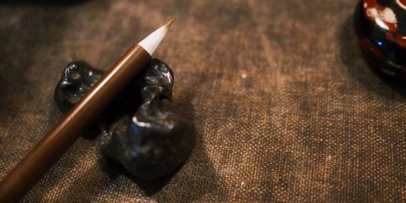 A fine-tipped calligraphy brush resting across a dark, irregularly shaped ceramic brush stand