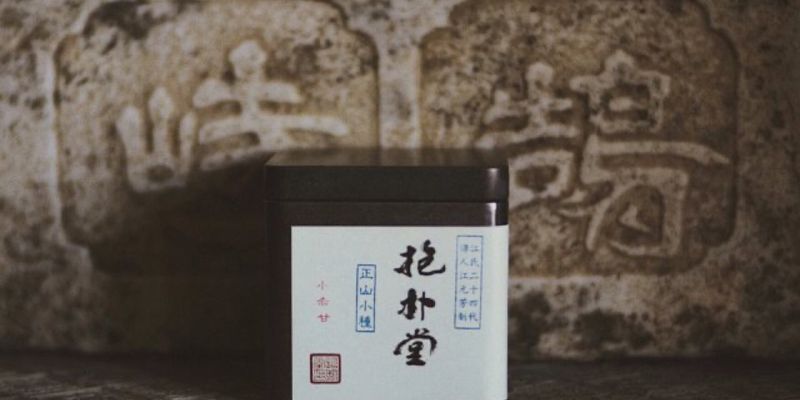 A dark tin of tea labeled in Chinese, set against a weathered stone carving of large characters