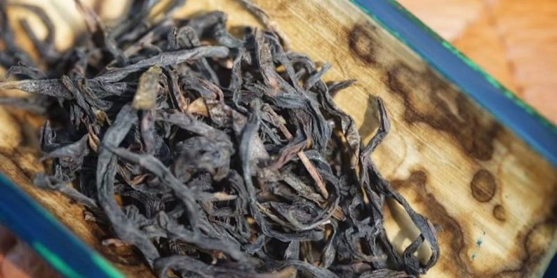 Loose dark oolong leaves resting on a wooden tray with worn, weathered edges