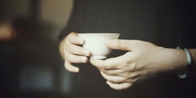 Two hands holding a small white porcelain gaiwan