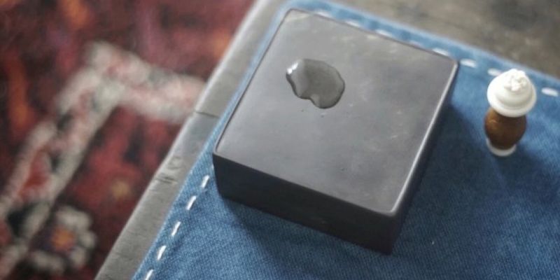 A small square black inkstone with a pool of ink in its well, resting on a woven blue fabric
