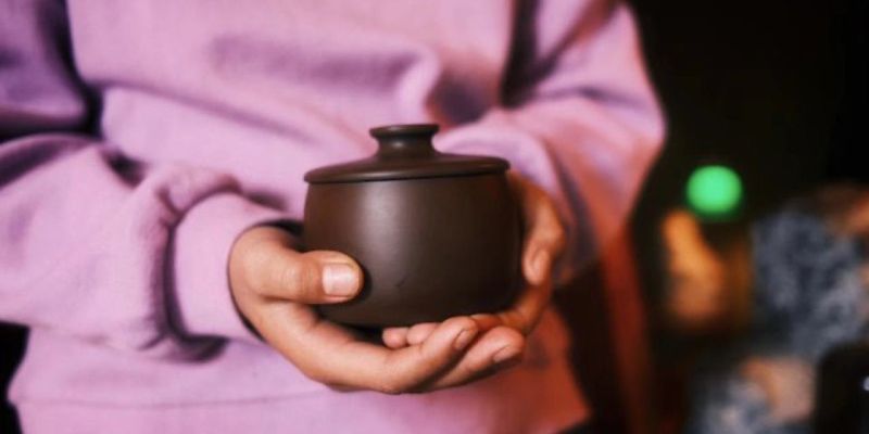 Hands holding a small dark clay lidded jar