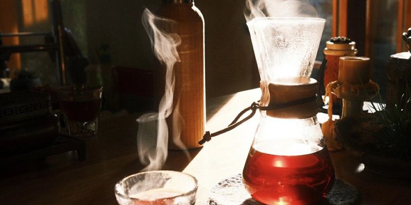 Steam rising from a glass teapot and cup of red tea, lit by late afternoon sun through a window