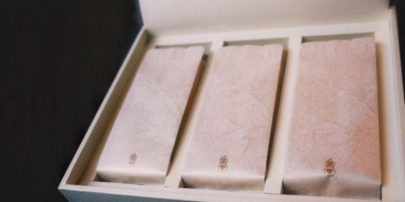 Three individually wrapped tea packets laid side by side inside an open gift box