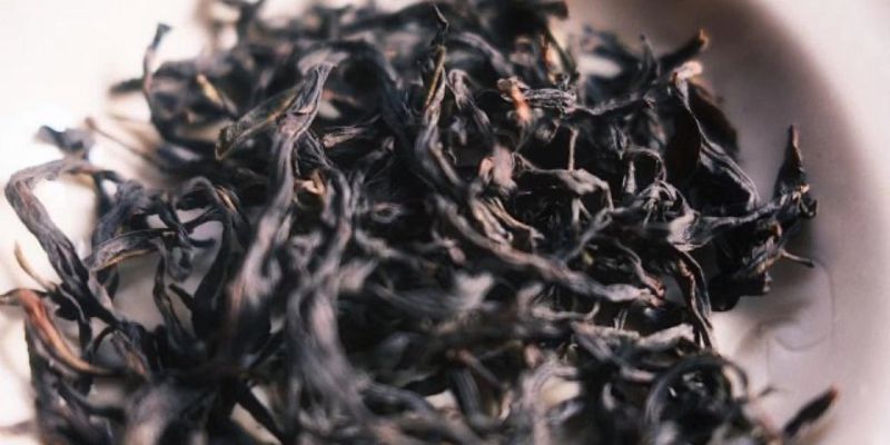 A close-up bowl of dark, tightly rolled oolong tea leaves