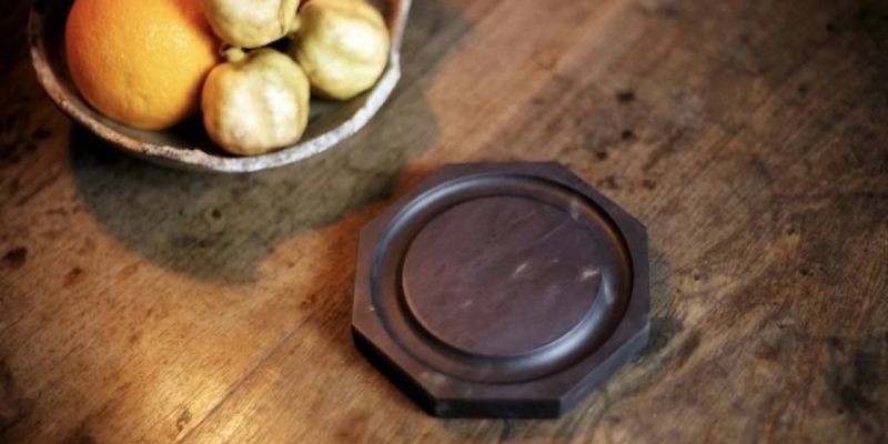An octagonal dark stone inkstone on a wooden table, beside a bowl of fruit