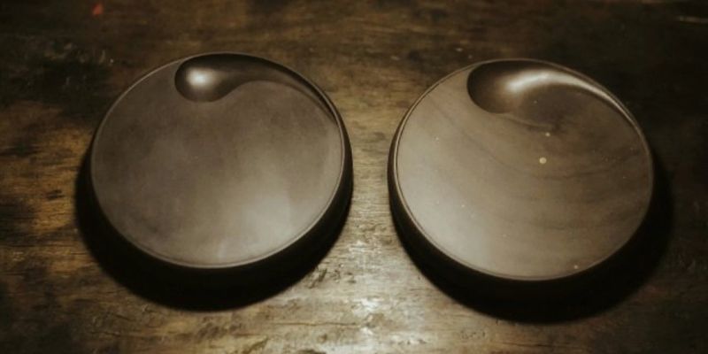 Two round dark inkstones with curved ink wells, photographed side by side on a wooden table