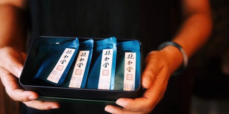 A pair of hands holding a small tin of four individually wrapped tea packets